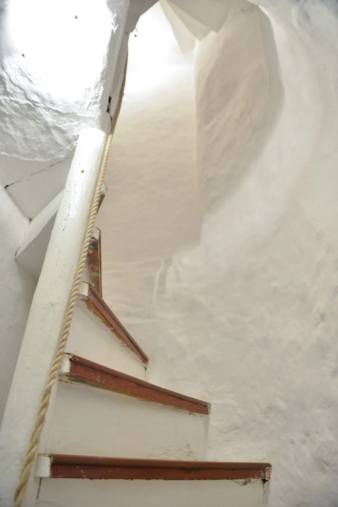 Die enge Wendeltreppe aus dem 14. Jahrhundert: weiß gestrichene Stufen mit rotem Kantenschutz, ein Seil als Handlauf, die gekalkte Wand windet sich nach oben.